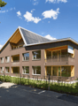 3 story building, brown exterior, solar panels on roof, multiple balconies, large windows