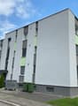 Modern apartment building with gray and green exterior, multiple windows, and a flat roof.