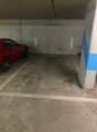 concrete floor, two doors on the wall with numbers, red car parked, empty parking area