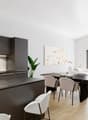 modern kitchen with marble countertop, stainless steel appliances, large dining table, modern chairs, white walls, wooden floor, large windows, plants