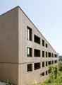 Modern wooden building, multiple windows, balconies, surrounded by greenery