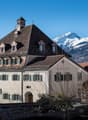large building with multiple windows, brown roof, stone walls, surrounded by mountains