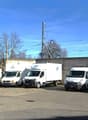 Several white vans parked in a lot with an electric pole and power cables.