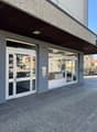 Exterior of a building with glass doors and windows, gray walls, and a paved entrance.