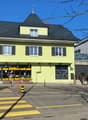 3 story building, yellow exterior, black roof, glass doors, windows, street view