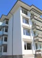 Multi-story residential building, white exterior, balconies on upper floors, large windows, modern architecture, grey stone accents, flat roof with ridge tiles