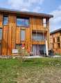 wooden exterior, large windows, balconies, outdoor seating area, green lawn, mountain view