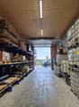 Warehouse with wooden shelves, metal racks, and storage boxes. Open door leading to a road with a van parked outside.