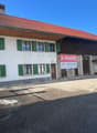 White and brown building, terracotta roof, multiple windows, two doors, sign indicating it is for sale