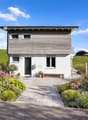 2 story house, wooden exterior, white walls, raised ground floor, garden, bench, mailbox