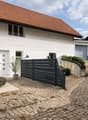 white house, brown roof, black gate, brick driveway, stairs, plants