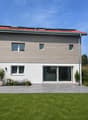 2 story house, wooden and white exterior, solar panels on roof, large glass doors, garden with plants