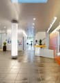 spacious lobby, light grey floor tiles, tall glass walls, white and orange walls, metal column, plants