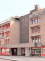 Multi-story commercial building with red accents, balconies, and retail spaces on the ground floor