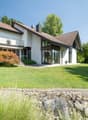 2 story white house, brown roof, balcony, stairs, green lawn, rocks, plants