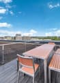 Outdoor wooden deck, dining table and chairs, metal railings, plants in pots, city skyline view