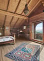 bedroom with wooden bed, rug, wooden wall and flooring, large window with wooden balcony, lamps, desk, bookshelves
