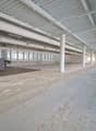Empty building with high ceiling, large windows, concrete floor, metal beams, and pipes