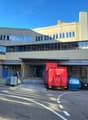 modern building with glass walls, raised ground floor,  blue entrance doors, cars parked in front
