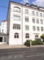 4 story building, white exterior, multiple windows, car parked in front, street with tram tracks