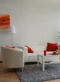 Living room, white couch, red pillows, armchair, floor lamp, coffee table, decorative items, window with curtains