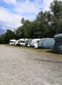 Multiple covered caravans parked in a gravel parking lot with trees in the background.