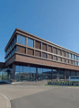modern office building, glass facade, spacious parking area, brown facade, cars parked in front, trees and bushes, sign with 'Reisezentrum'