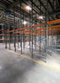 Empty warehouse with metal shelving units, concrete floor, yellow line on the floor, windows on the left side, metal beams on the ceiling