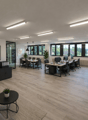 modern office space with wooden floors, large windows, desks, chairs, plants, motivational quote on wall