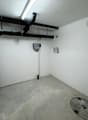 Empty room with concrete floor, white brick walls, pipes, and a drain cover