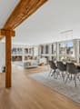 open living room with dining area, large windows, wooden floor, wooden beam, table, chairs, rug, side table, couch, coffee table, pillows