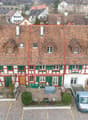 2-story building with red tiled roof, red and white color scheme, green shutters, and a small courtyard in the front