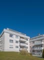 Modern apartment building, white exterior, multiple balconies, landscaped garden, driveway