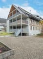 modern house, 3 stories, large balcony, metal railings, grey gravel driveway, mountain in background