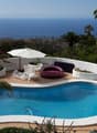 Pool with slide, lounge area with chairs and umbrella, garden with plants and trees, ocean view