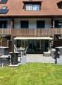 2 story house, brown roof, solar panels, wooden balcony, outdoor seating area, garden, patio