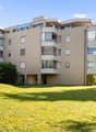 Apartment building, beige bricks, many balconies, glass windows, surrounded by trees