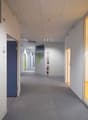 Empty hallway with gray carpeted floor, white walls, ceiling with lights, blue and green doors, and fire extinguisher