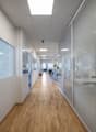 Office hallway with wooden flooring, glass partitions, and overhead lighting.