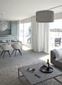 Open-concept living room and kitchen with large windows providing a scenic view. The living room features a grey sofa with decorative pillows, a coffee table, and a shag rug. The kitchen has grey cabinets, a dining table with white chairs, and a modern pe