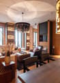 Fireplace, chandelier, couch, armchairs, side table, coffee table, rug, lamps, wooden floor, wood-paneled walls