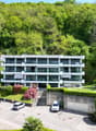 3 story apartment building, white exterior, large windows, balconies, parking area, green surroundings