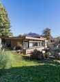 modern-style house, yellow walls, 3-story, large windows, outdoor seating, lawn, trees, mountains in background