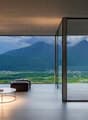 Spacious living room with large floor-to-ceiling windows offering a stunning view of the mountainous landscape outside. The room features a comfortable sofa, a coffee table, and an armchair, creating a cozy and relaxing atmosphere. The minimalist and mode