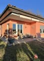 Single-story house, brick walls, red roof, large windows, outdoor seating area, garden, patio