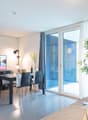 Spacious living room with large windows, balcony, dining table, TV stand, and potted plants