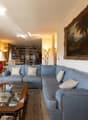 large blue sofa, glass coffee table, wooden cabinet, bookshelves, large window, painting