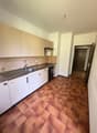 Modern kitchen with white cabinets, tiled countertops, stainless steel sink, and appliances. Brown tiled flooring.