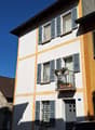 multistory building, white and yellow, four floors, balcony with plants, two windows on each floor