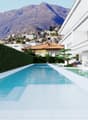 Modern house with a large swimming pool, surrounded by a lush garden and overlooking a mountainous landscape. The house has a sleek, white exterior with large windows and a terrace.